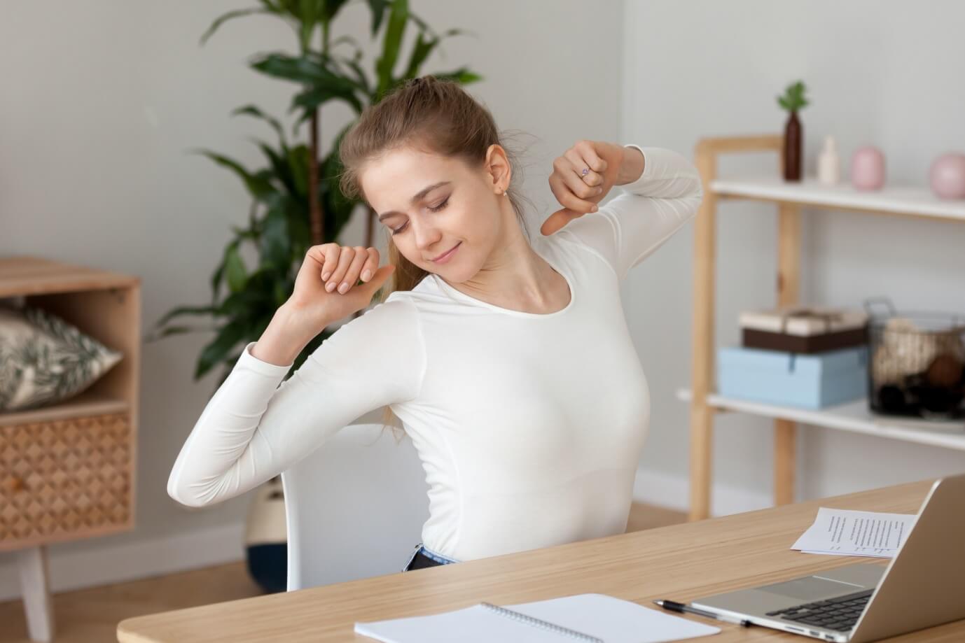 Woman sitting at desk stretching.
